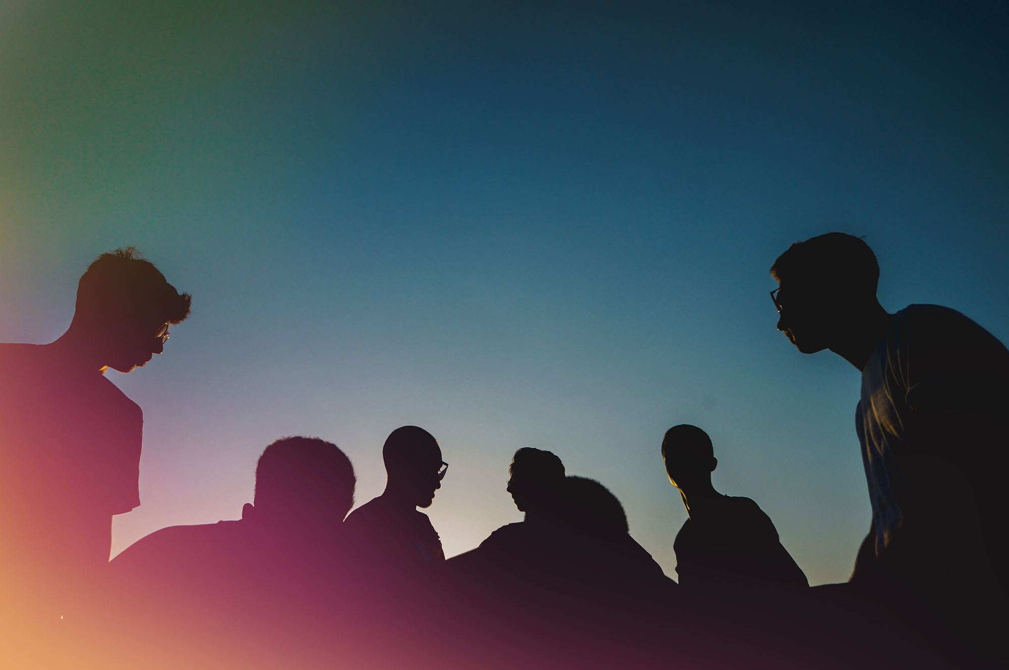 a stylized low-angle photograph of a group of people standing against an evening sky in silhouette. 