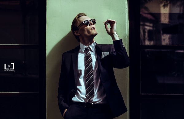 Aidas, an actor is dressed sharp in front of a bright wall.A. Gudas Fotografija