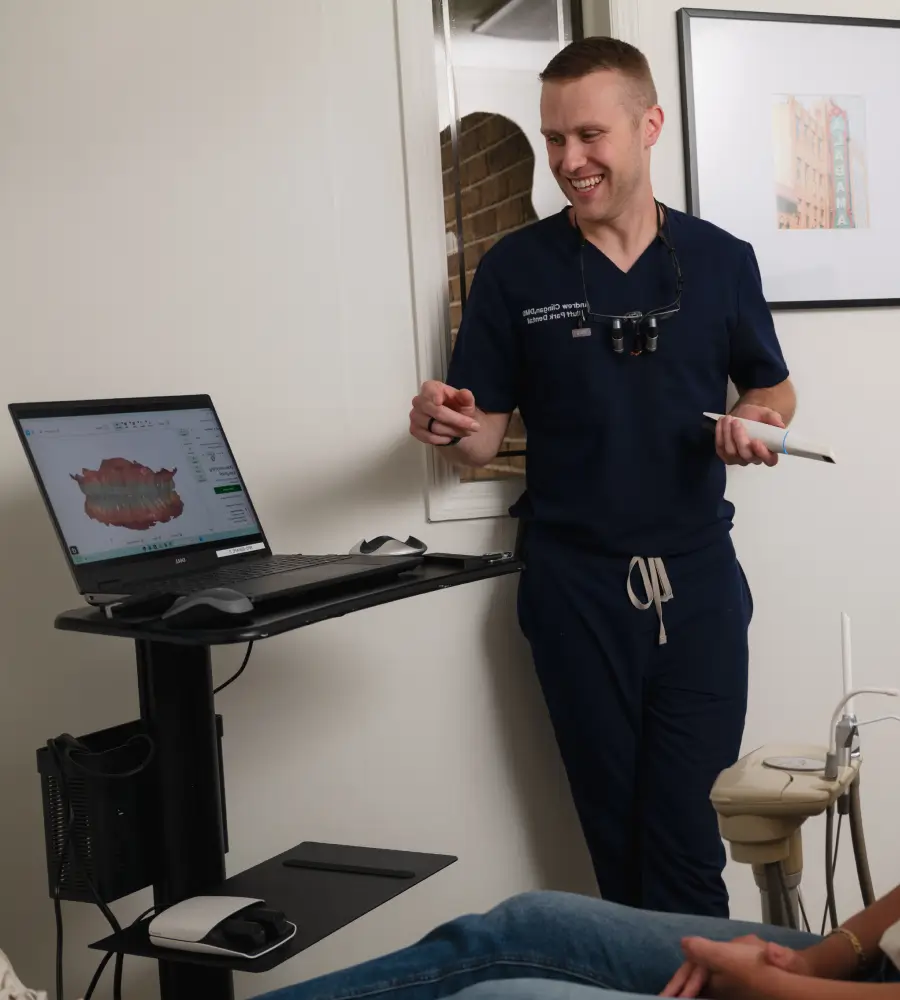A dentist shows a dental scan on a laptop to a patient sitting in a dental chair.