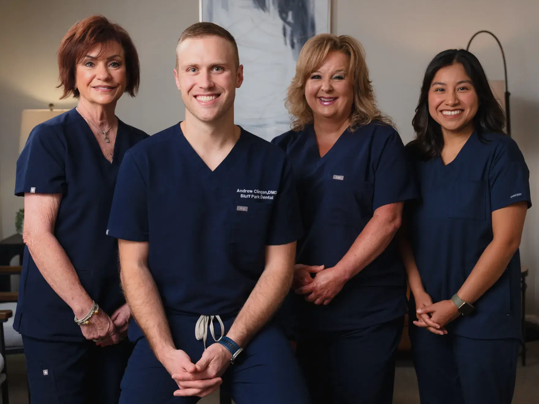 Four people in navy scrubs smile while standing and sitting in an office setting.