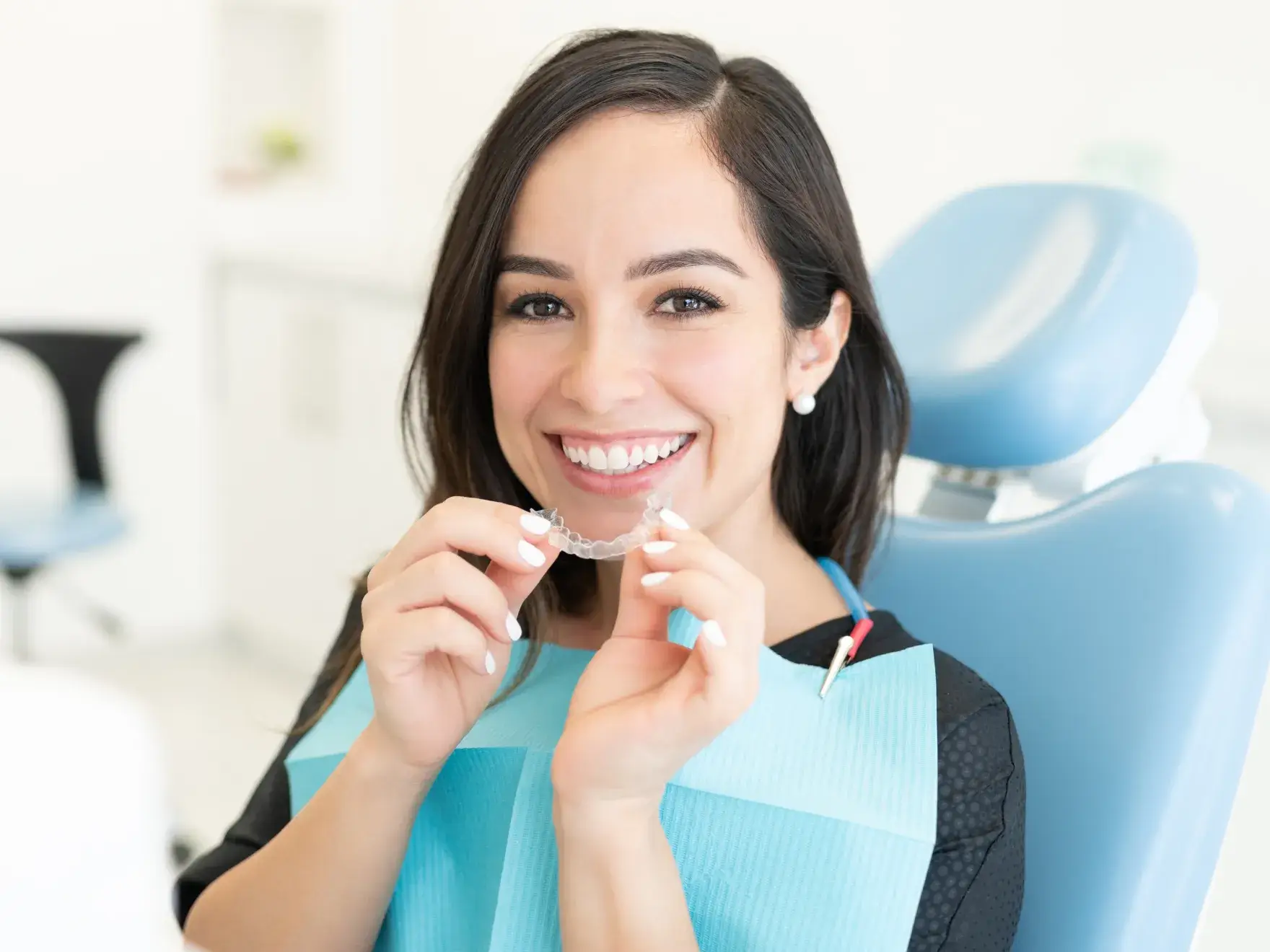 A woman sitting in a dentist chair holding a clearaligner.