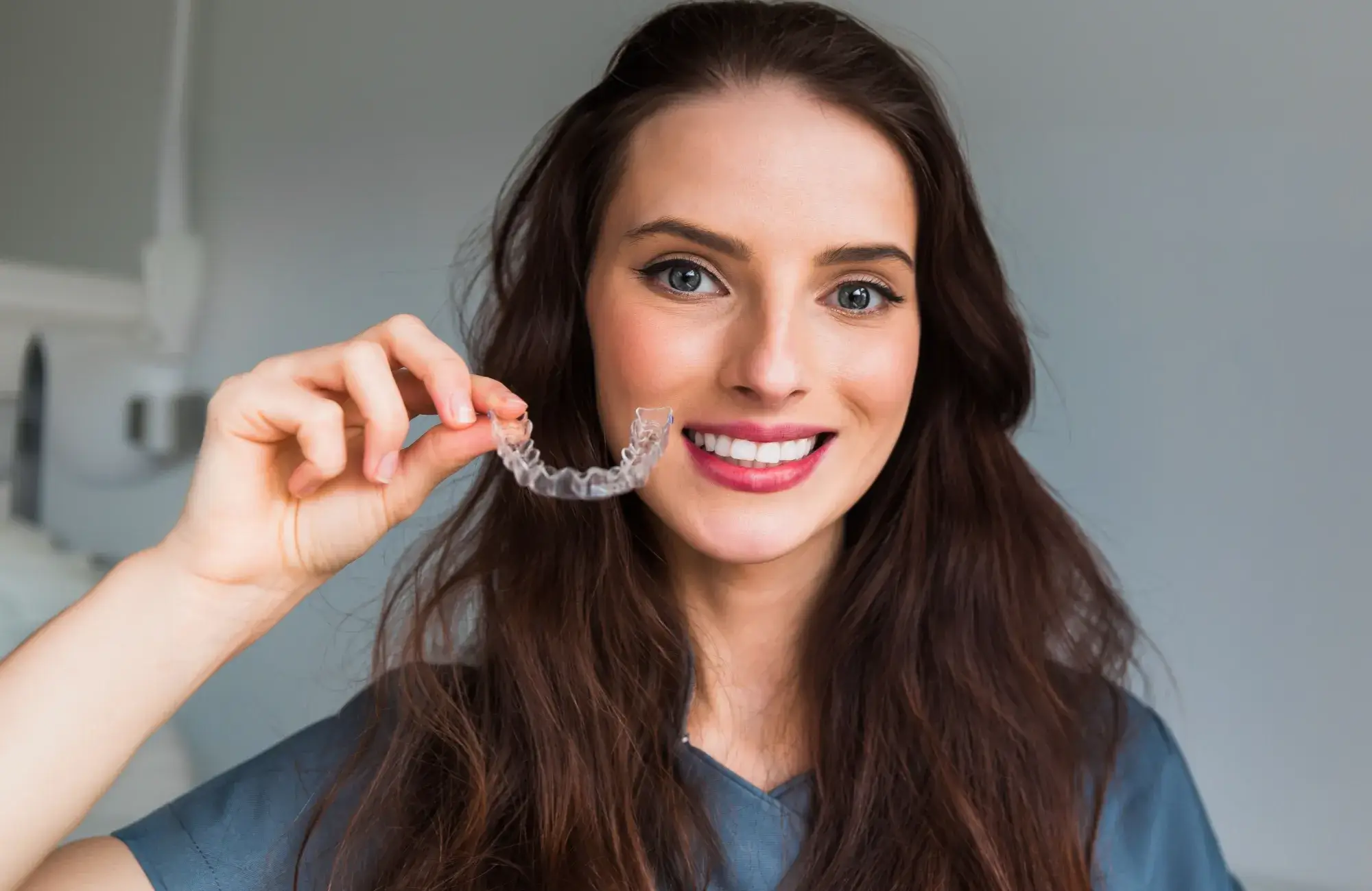 A woman holding a clearaligner to her teeth.