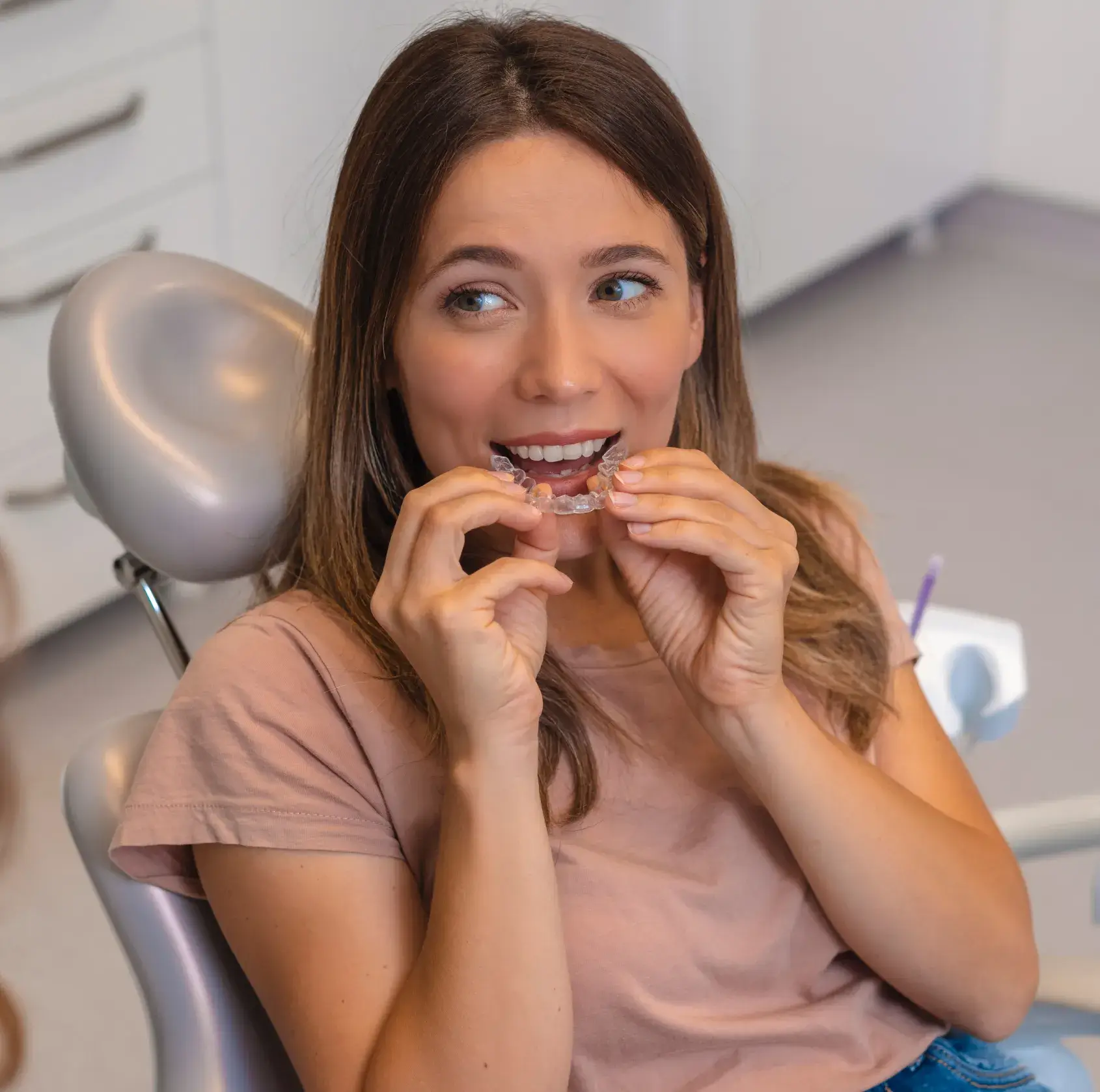 A woman sitting in a chair with a clearaligner in her mouth.