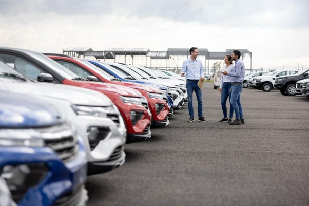 Three people talking on a car dealership lot