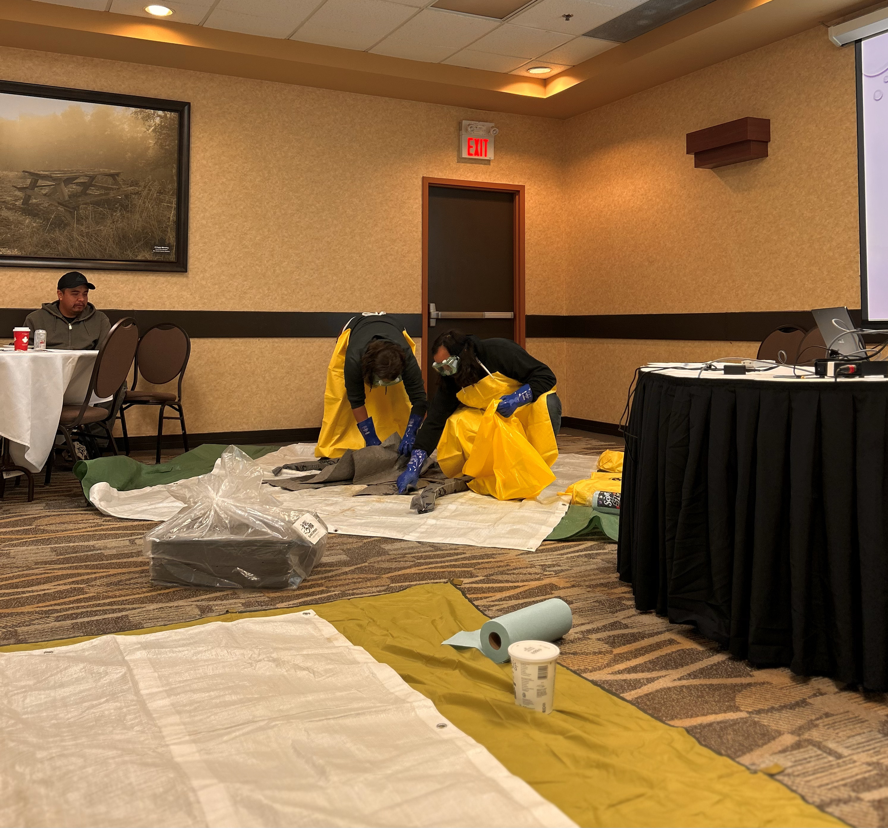 Two people dressed in safety equipment demonstrate a hazardous waste spill protocol.