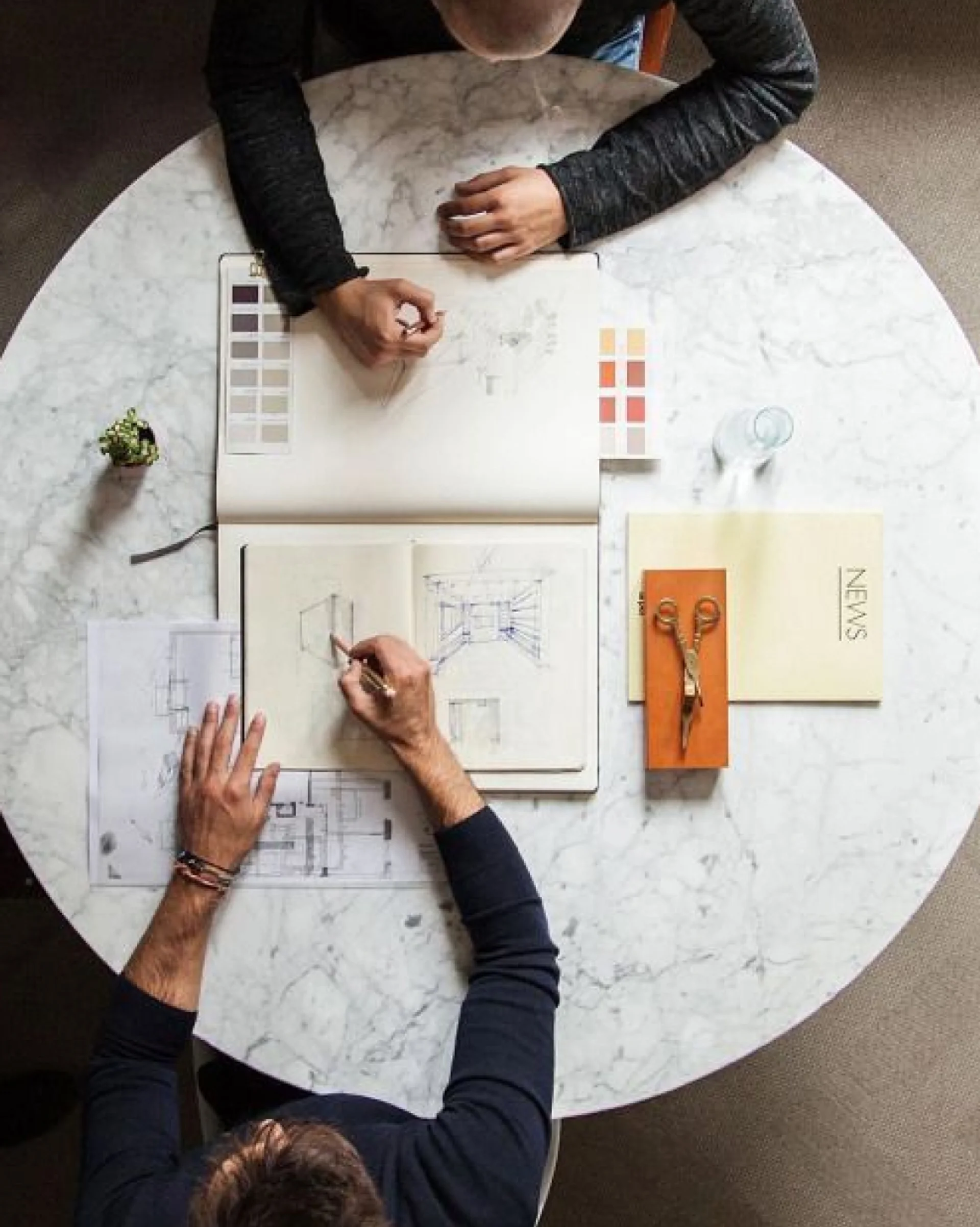 Two people working on architectural sketches and color swatches at a round marble table.