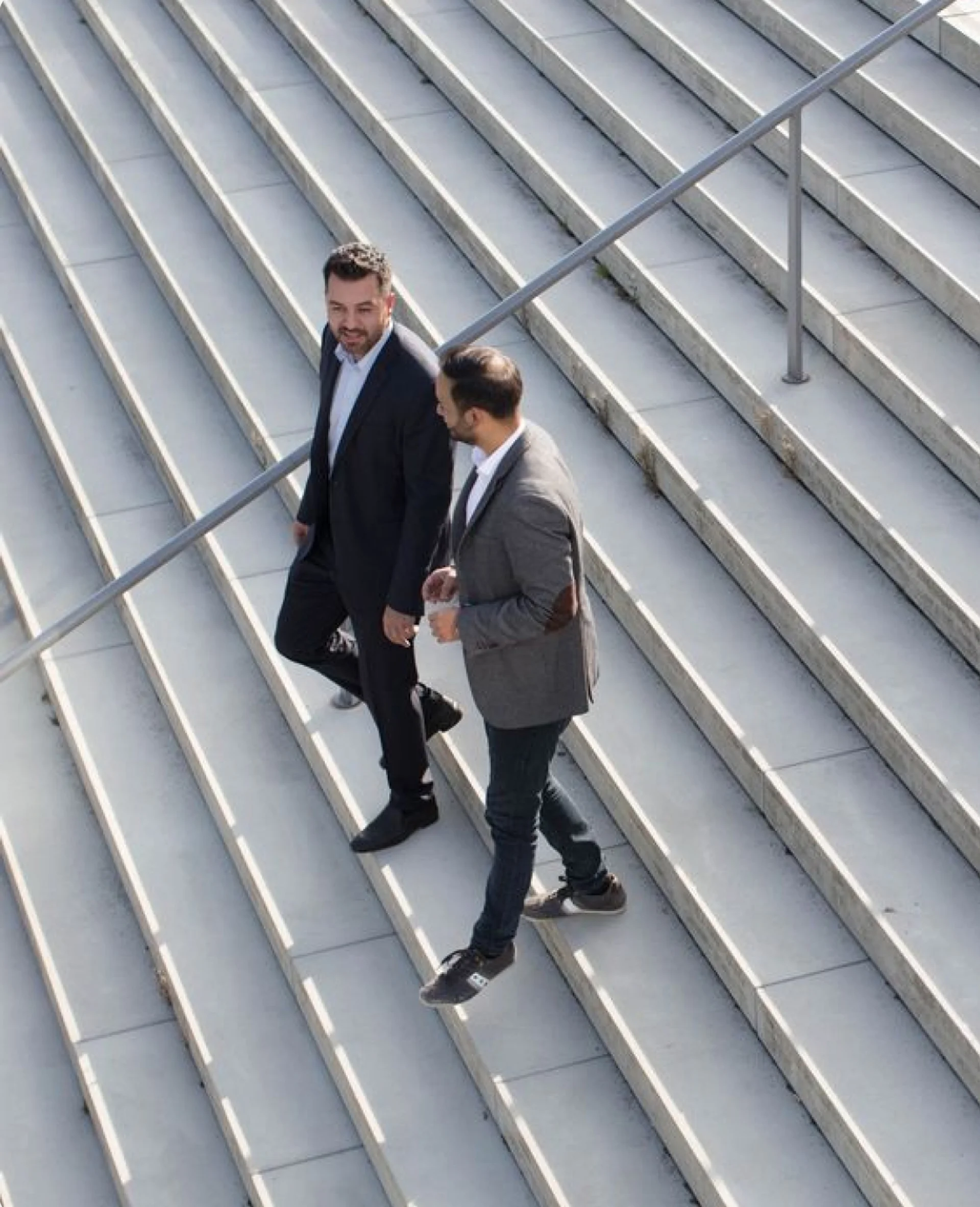 Two men in business casual attire walking down concrete outdoor stairs while talking.