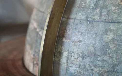Close-up of a vintage globe showing faded map details and a brass meridian on a wooden base.