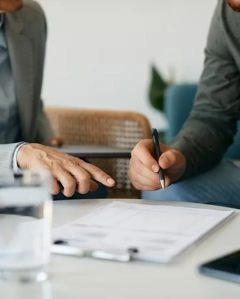Two people at a table reviewing and pointing at a document with a pen.