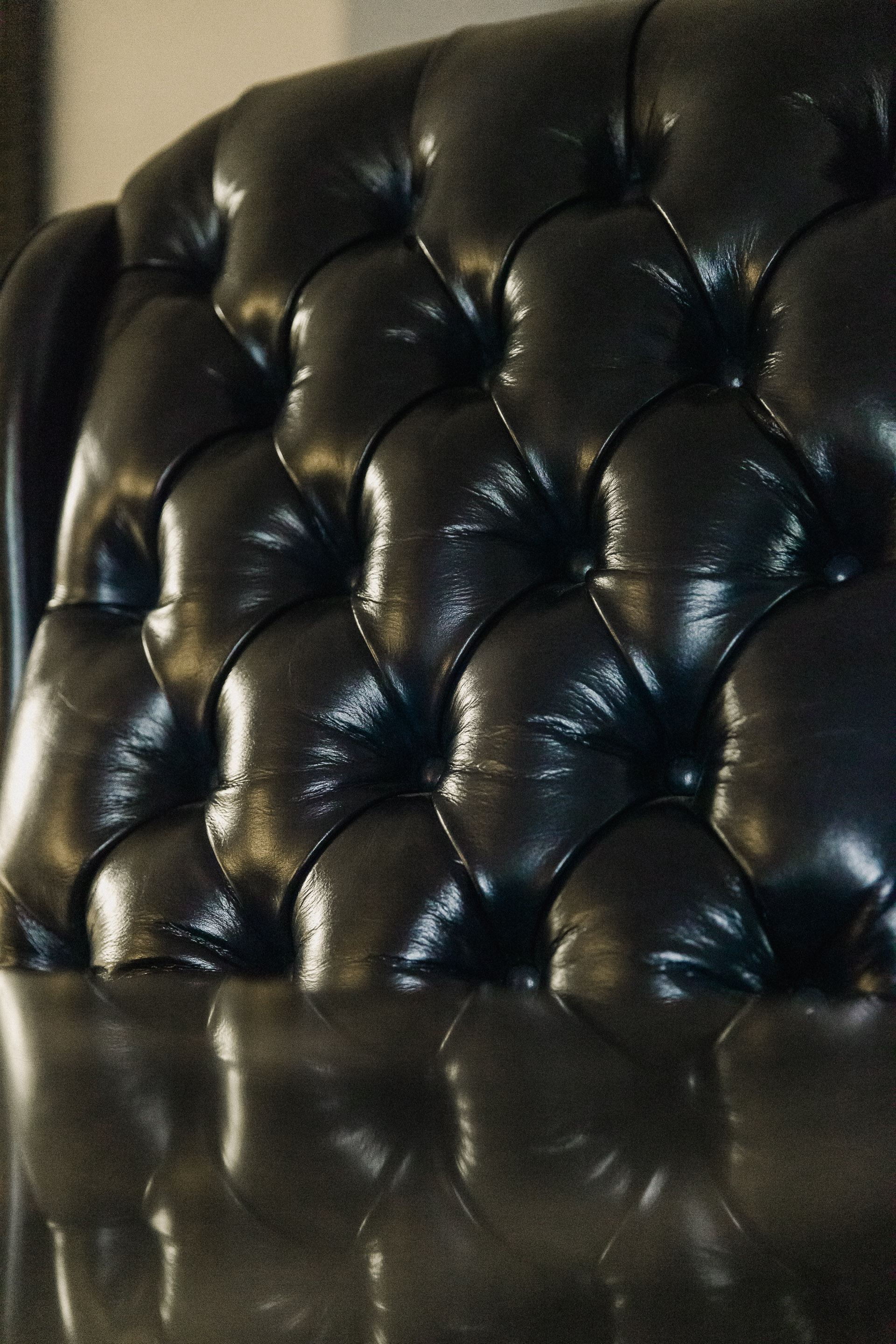 Close-up of black tufted leather couch with glossy finish reflecting light.
