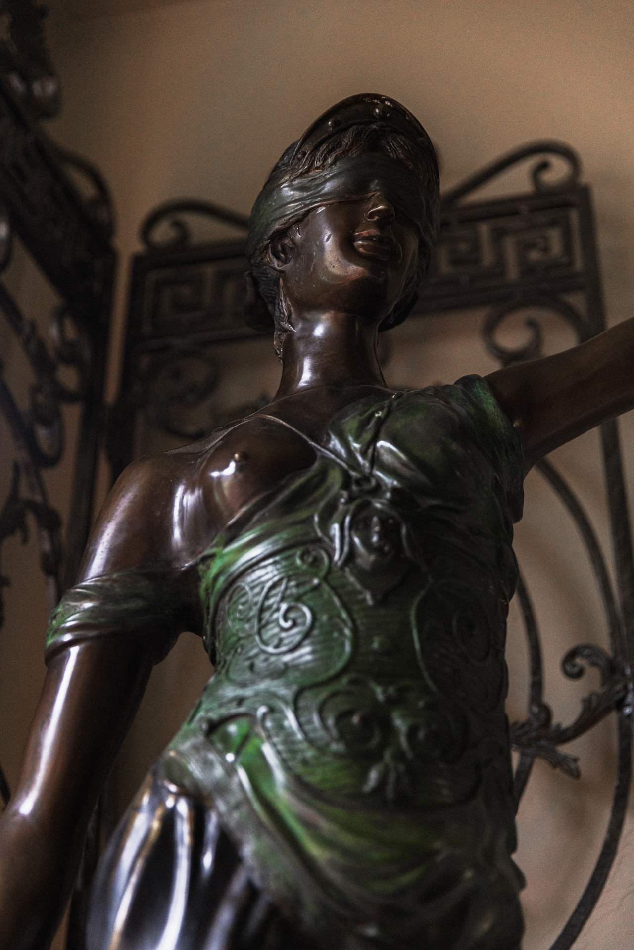 Bronze statue of a blindfolded woman wearing an intricately detailed green dress.