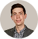 Portrait of a young man wearing a dark blazer and checkered shirt, smiling against a white background.