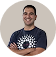 Smiling man with short hair wearing a dark t-shirt with a white circular pattern, standing against a white background.