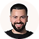 Smiling man with short dark hair, beard, and black t-shirt against a white background.