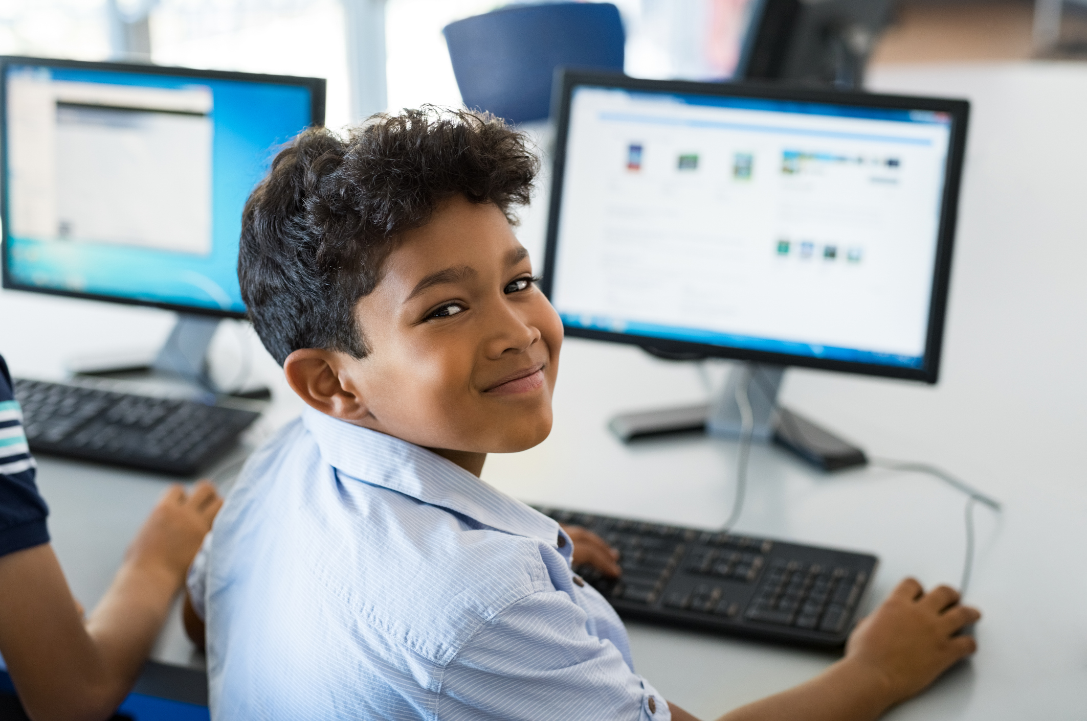 Young happy schoolboy using computer.