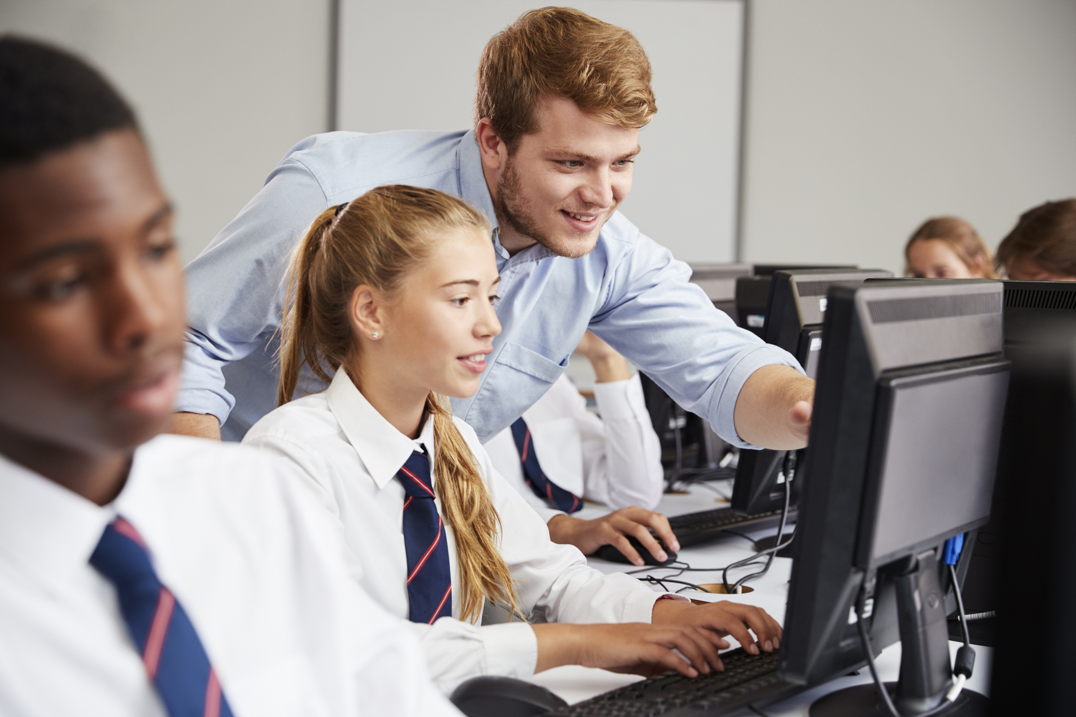 Two pupils are sitting behind computers receiving help in a lesson