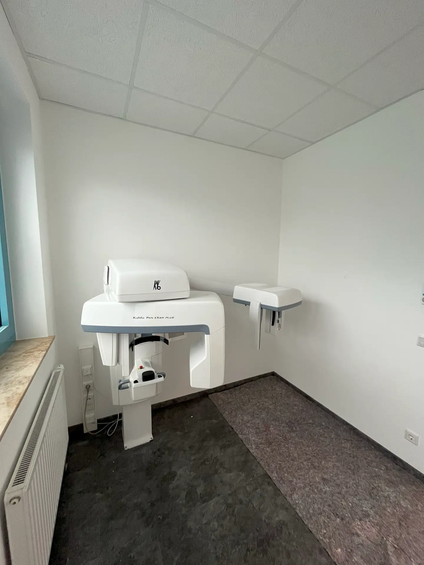 Fertig sanierter Raum mit weißen Wänden und dunklem Boden. Im hinteren Teil des Raumes ist ein medizinisches Gerät zu sehen.