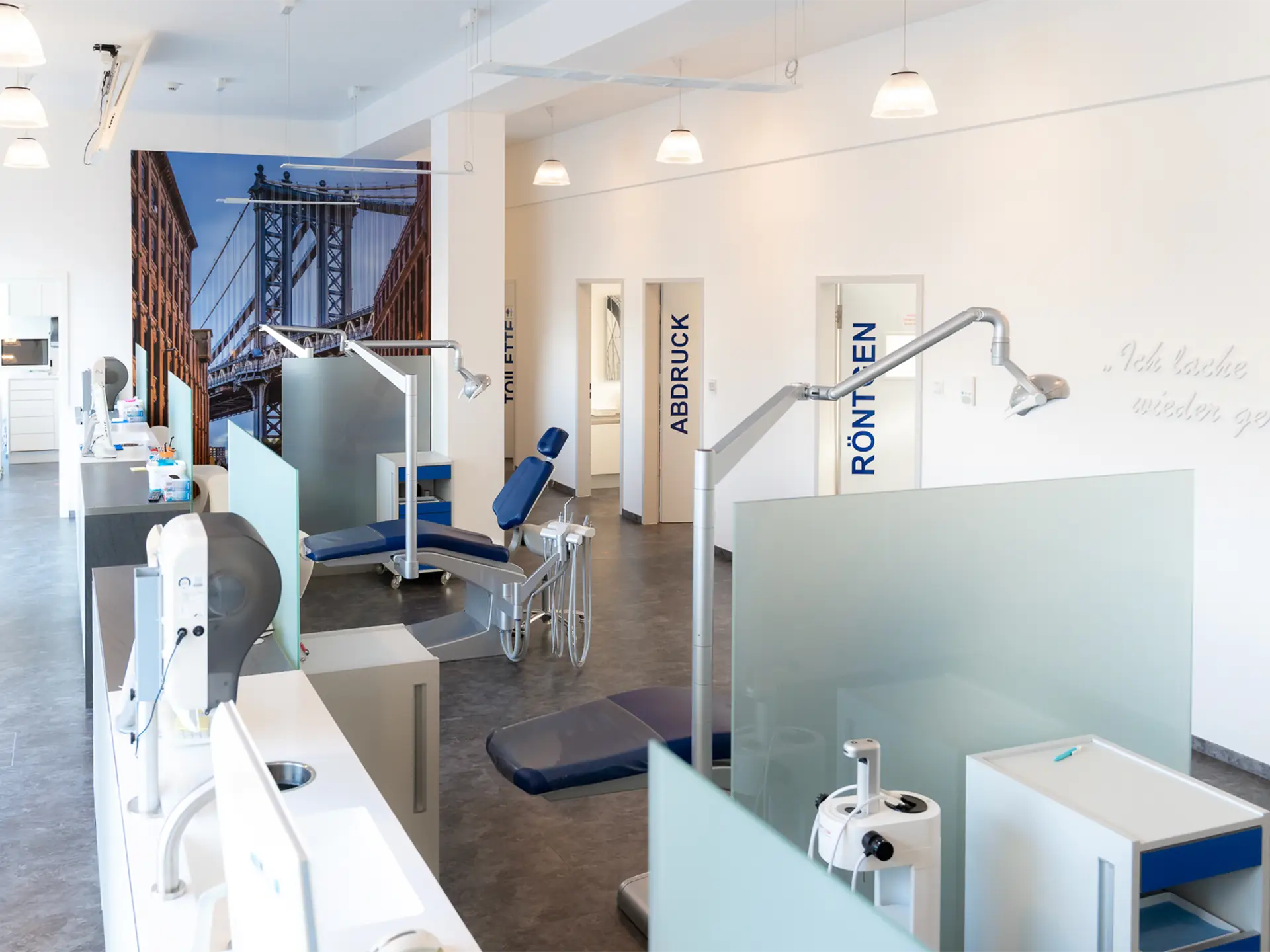 Fertig sanierte Praxisräume mit mehreren Behandlungssektionen, die durch undurchsichtige Glaswände getrennt sind. Der Raum ist hell erleuchtet, im Hintergrund sind Glastüren mit Beschriftungen zu sehen, die in anliegende Behandlungszimmer führen.