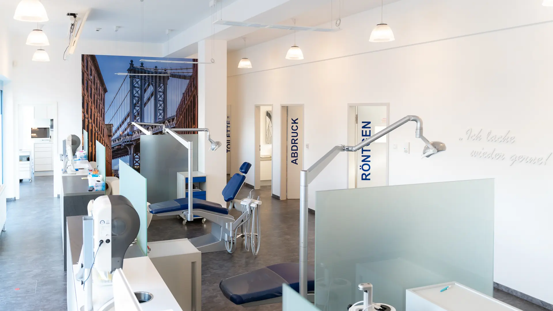 Fertig sanierte Praxisräume mit mehreren Behandlungssektionen, die durch undurchsichtige Glaswände getrennt sind. Der Raum ist hell erleuchtet, im Hintergrund sind Glastüren mit Beschriftungen zu sehen, die in anliegende Behandlungszimmer führen.