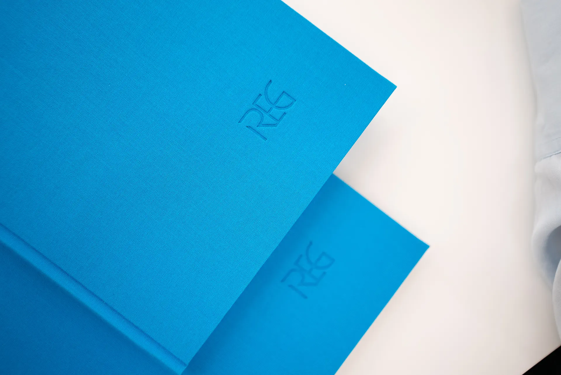 Zwei blaue Notizbücher übereinander, mit dem eingeprägten Schriftzug 'REG' auf der Vorderseite.