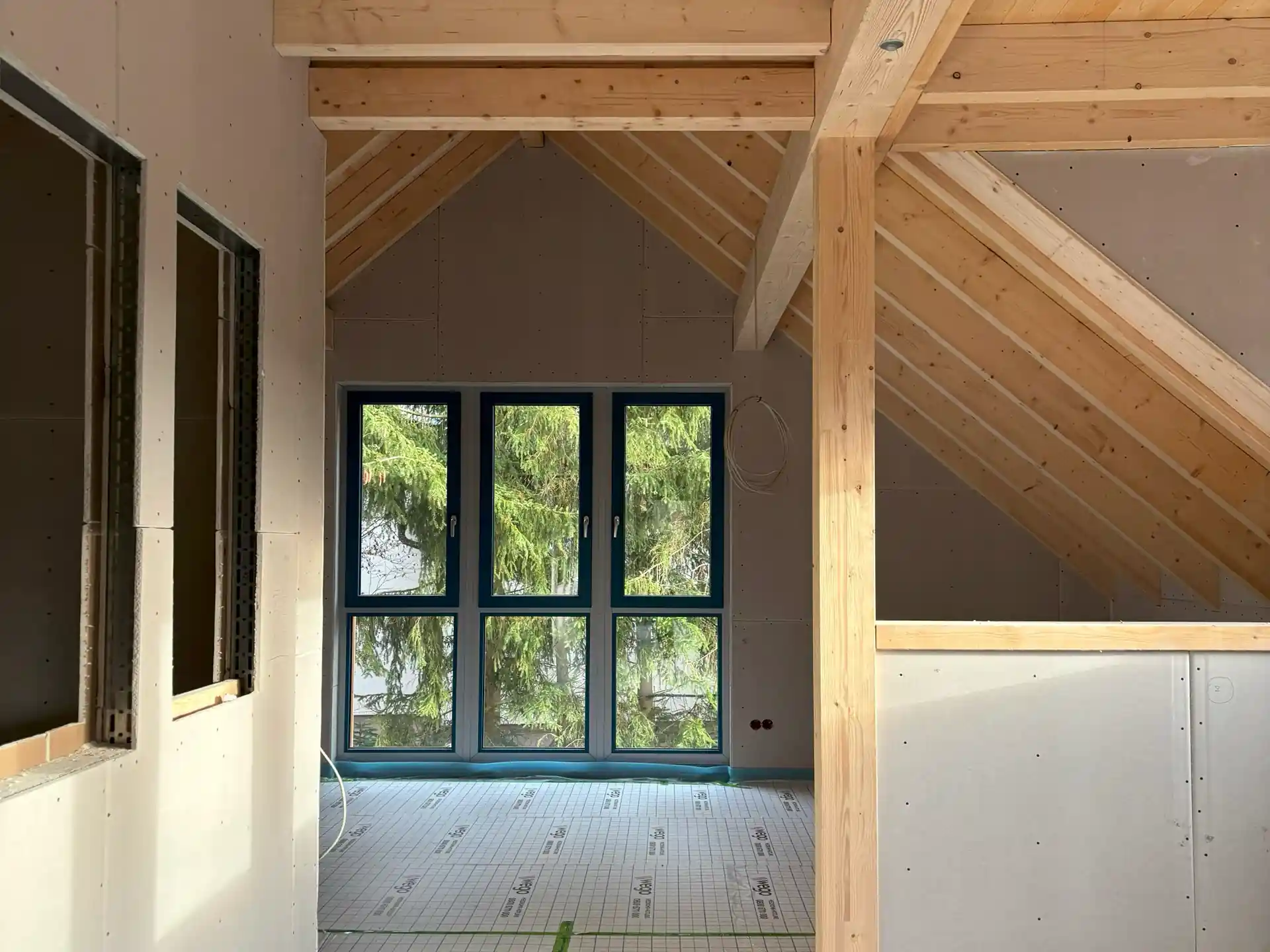 Innenraum einer sanierten Dachgeschosswohnung mit sichtbaren Holzbalken, neuen Fenstern und teilweise verkleideten Wänden während der Sanierung nach Brandschaden.