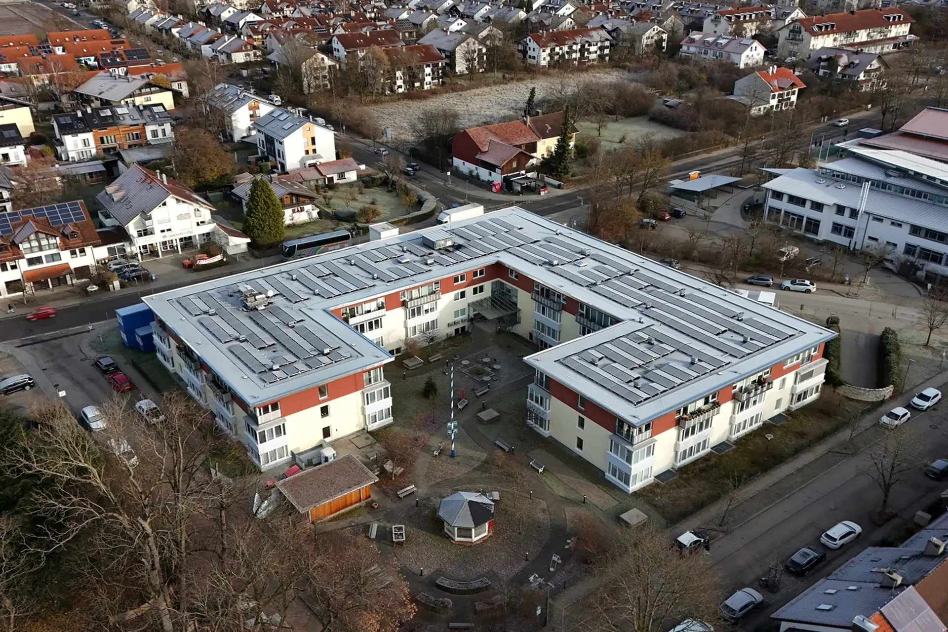 Luftaufnahme eines großen, flachen Wohngebäudes, umgeben von weiteren Wohnhäusern und Bäumen.