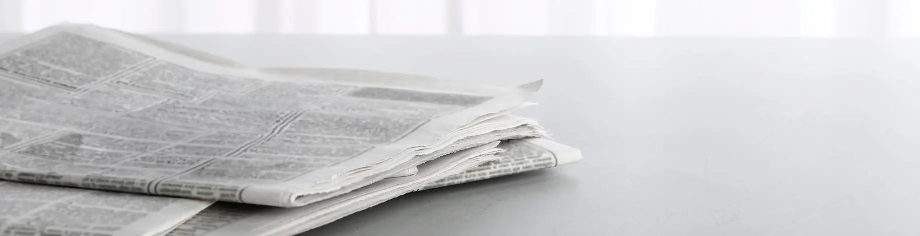 Gestapelte Zeitungen liegen auf einem weißen Tisch.
