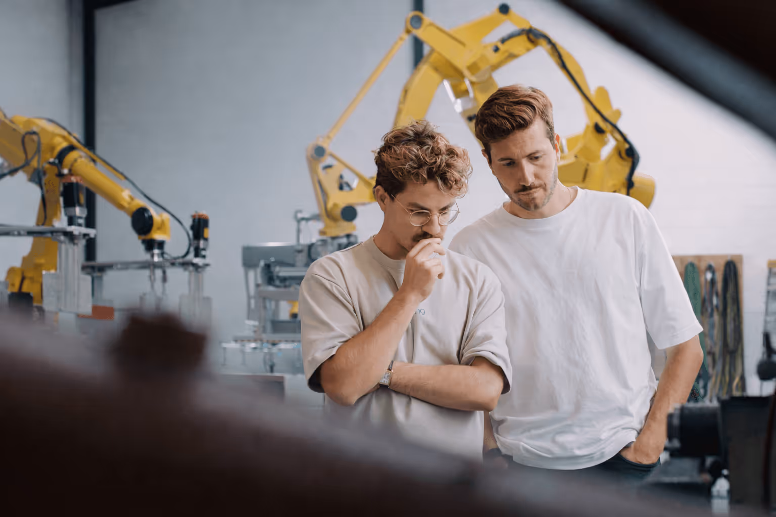 Zwei denkende Männer in einem Industriebetrieb vor Maschinen.