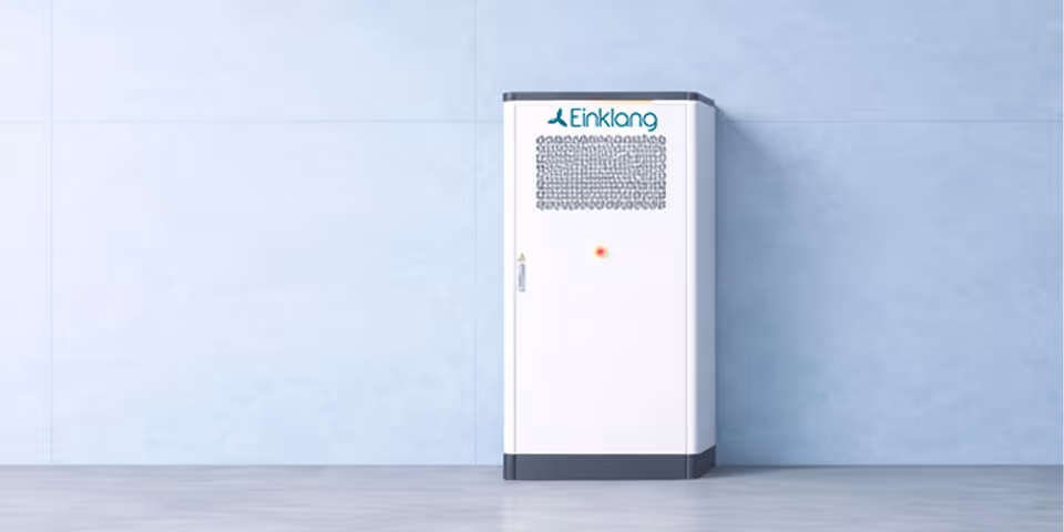 Weißer elektrischer Energiespeicher mit dem Logo Einklang vor einer blauen Wand.