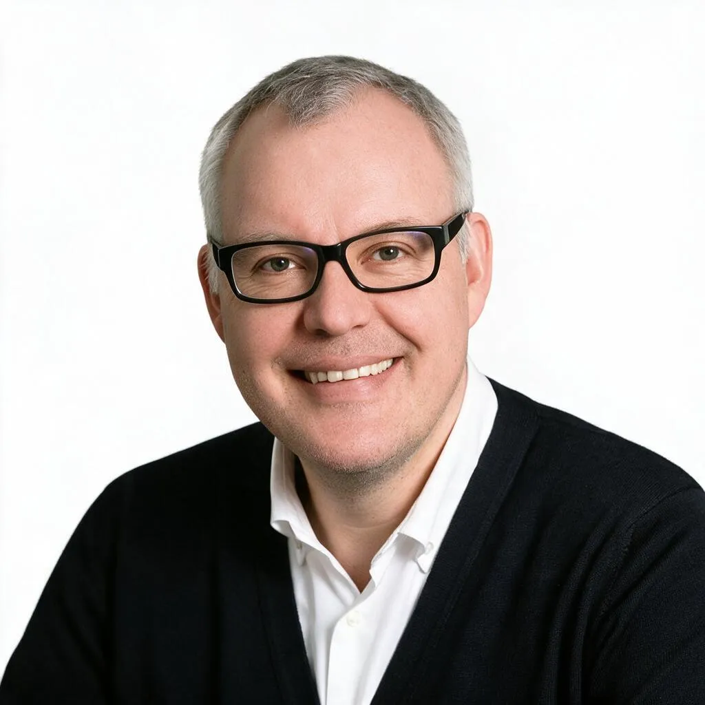 Porträt eines lächelnden Mannes mit grauem Haar, schwarzer Brille, weißem Hemd und schwarzem Pullover. Auf dem Bild ist Dr. Michael Wenzel abgebildet.
