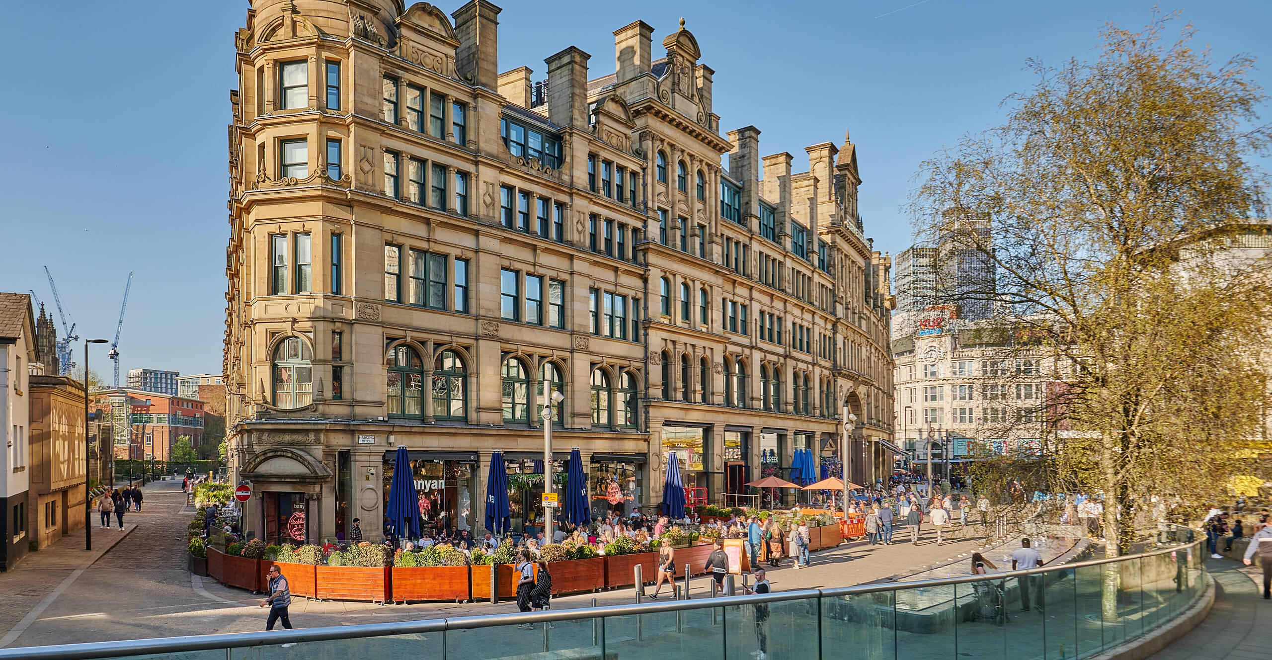 Historic Manchester building with bustling outdoor cafe and modern city backdrop