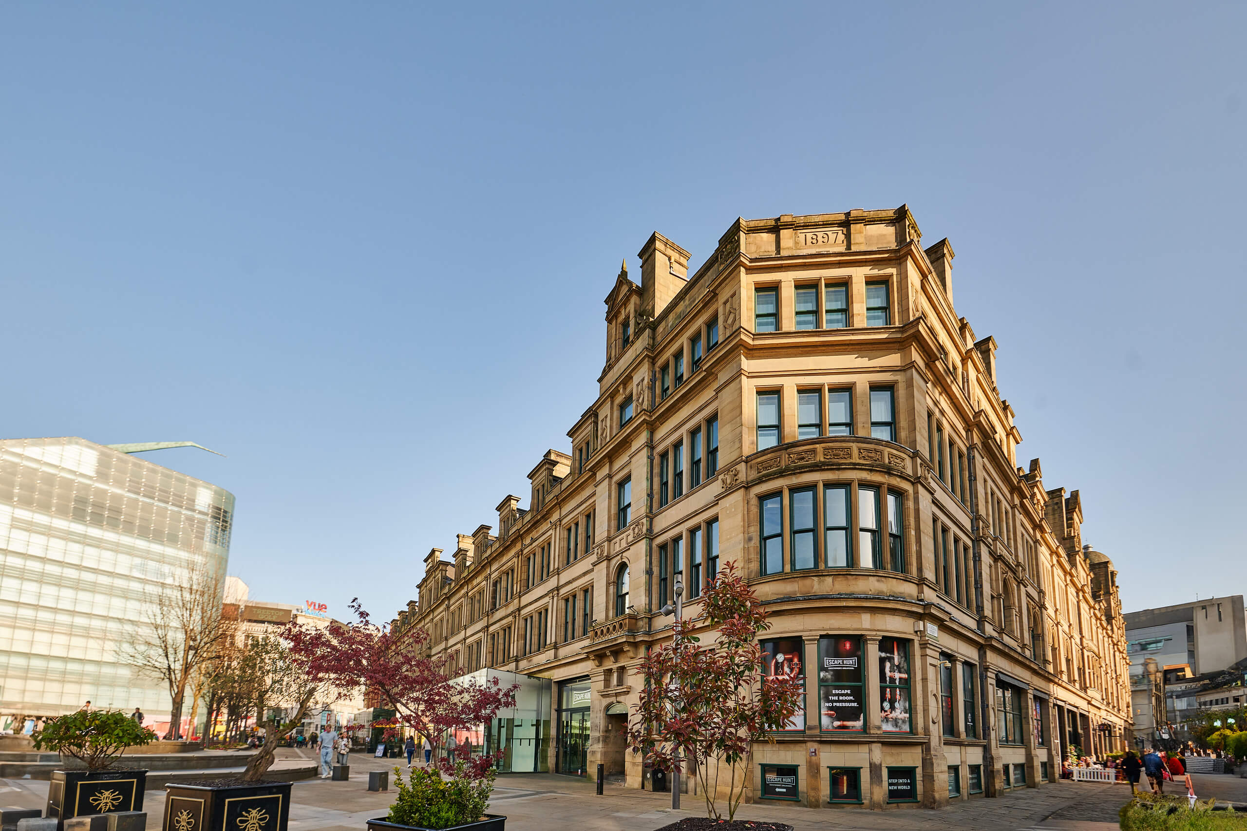 Historic sandstone building with 1897 date, modern city street, spring trees