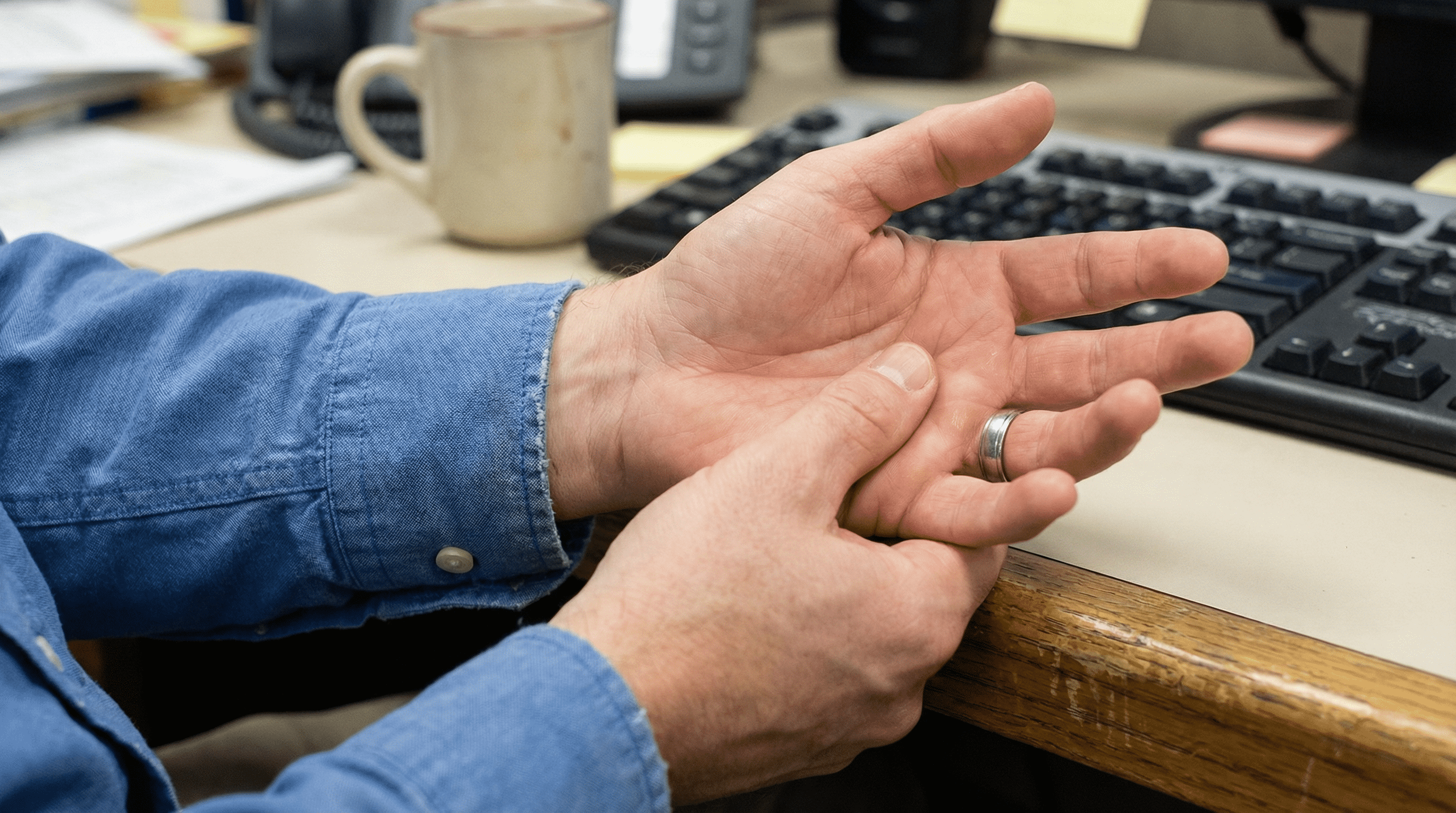 Close-up wrist on desk edge, person rubbing ring and little fingers.