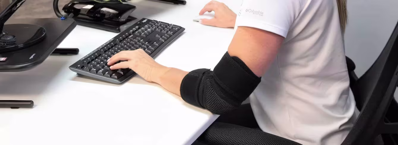 Woman adjusts counterforce elbow strap while using a mouse in UK home office.