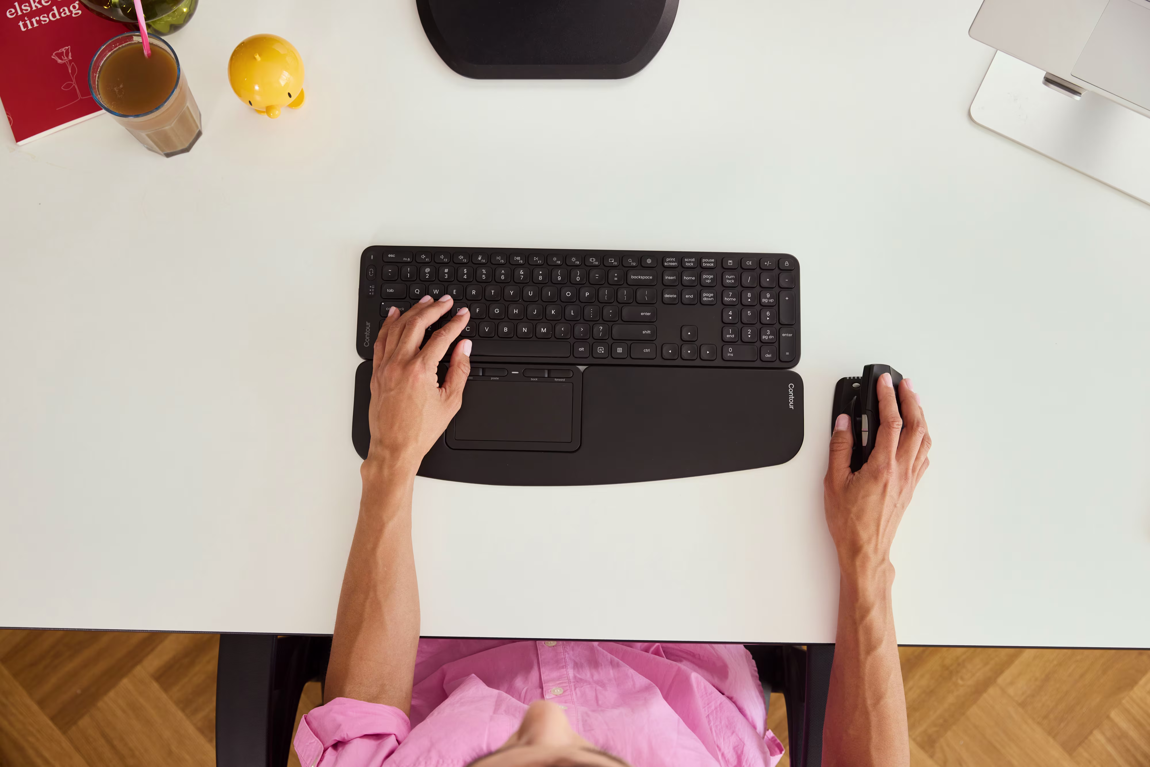 Ylhäältä kuvattu ergonominen kotitoimisto, jossa näppäimistö, rannetuki ja hiiri on sijoitettu neutraalia ryhtiä ja vähäisempää toistorasitusta varten.