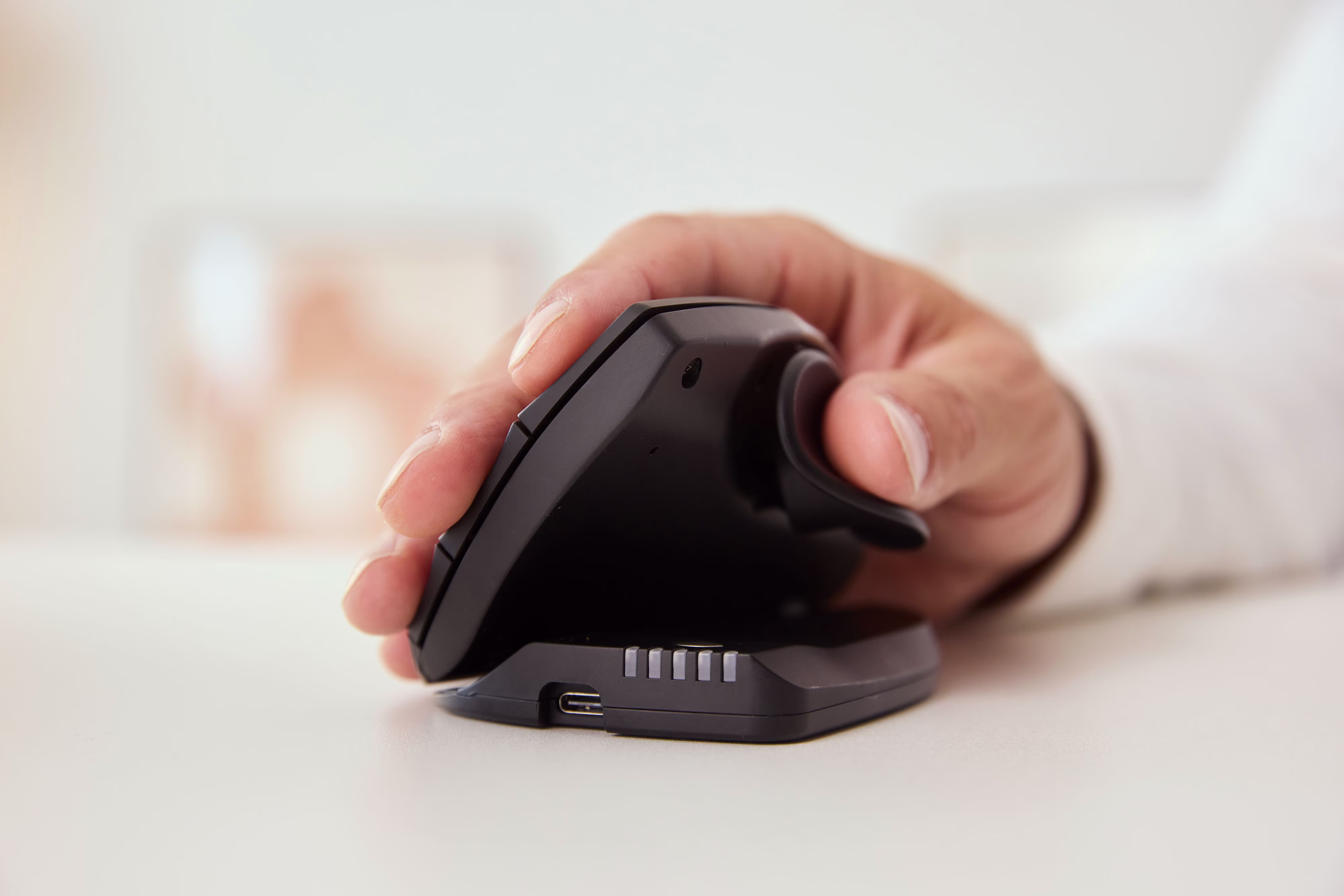 Hand som använder en vertikal ergonomisk mus, utformad för att främja en naturlig handledsställning vid datorarbete.