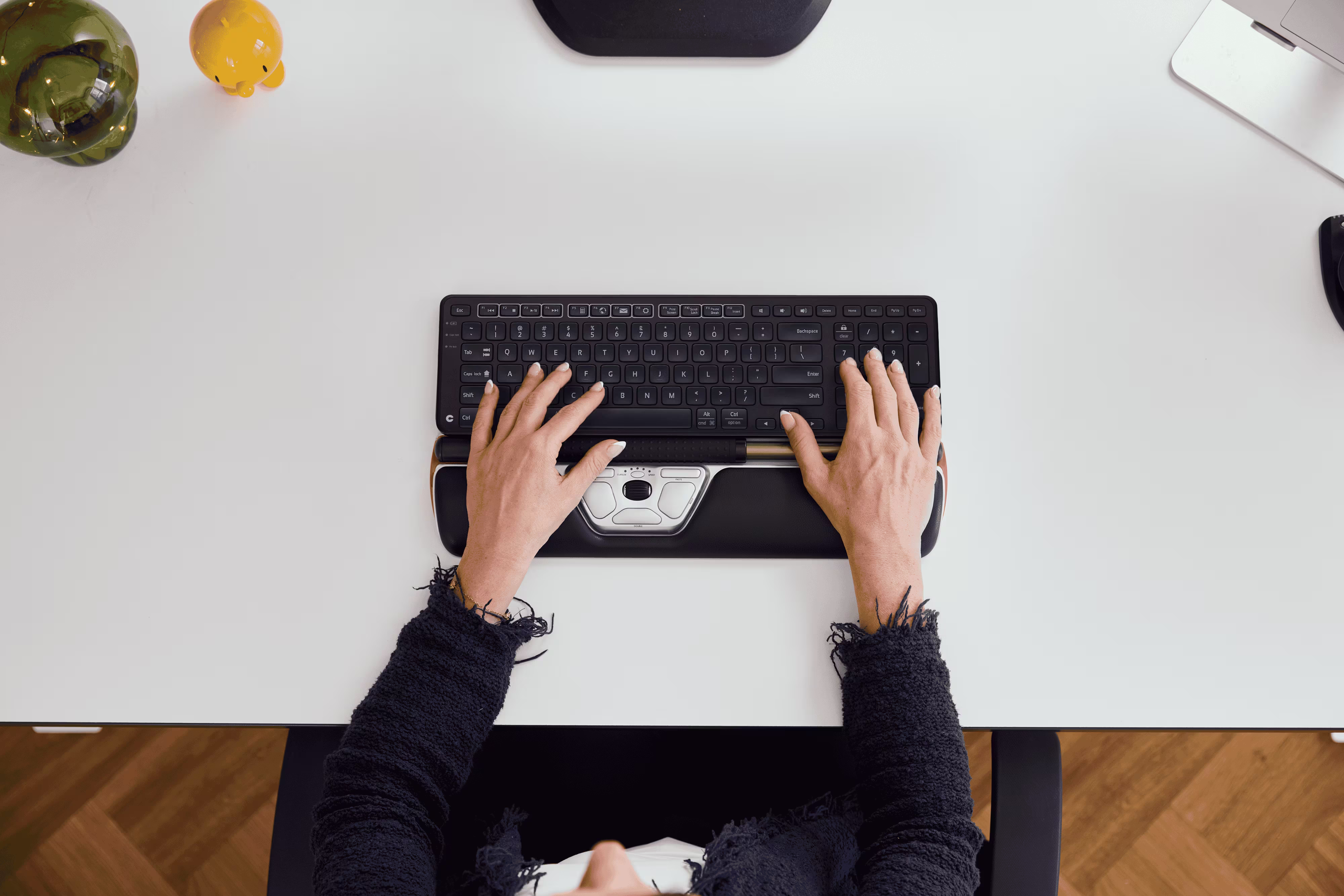 Ovanifrån: en användare skriver på ett ergonomiskt tangentbord parat med en centrerad RollerMouse Red med underarmsstöd för att minska belastningen på handleder och armar.