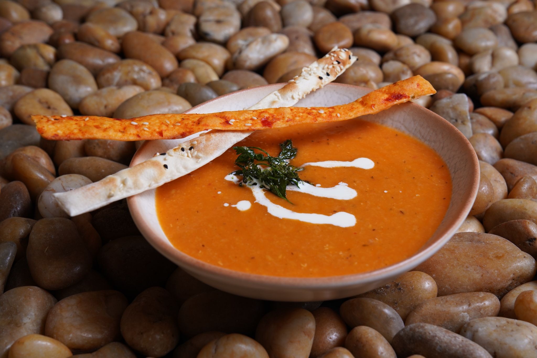 Bowl of creamy orange red lentil soup garnished with a cream swirl and chopped herbs