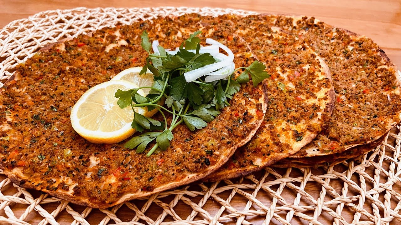 Stack of Turkish lahmacun — thin, round flatbreads topped with minced meat and vegetables, garnished with lemon slices, parsley, and sliced onion