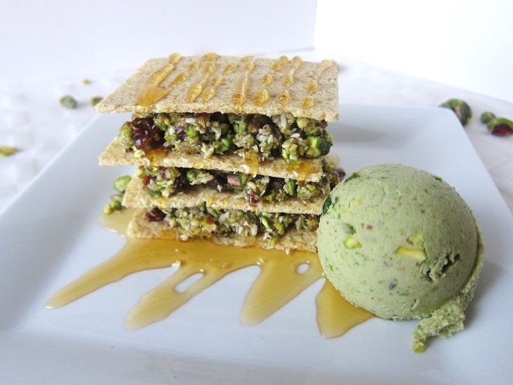 Stacked layers of crispy pistachio baklava drizzled with honey syrup, served on a white plate alongside a scoop of pistachio ice cream