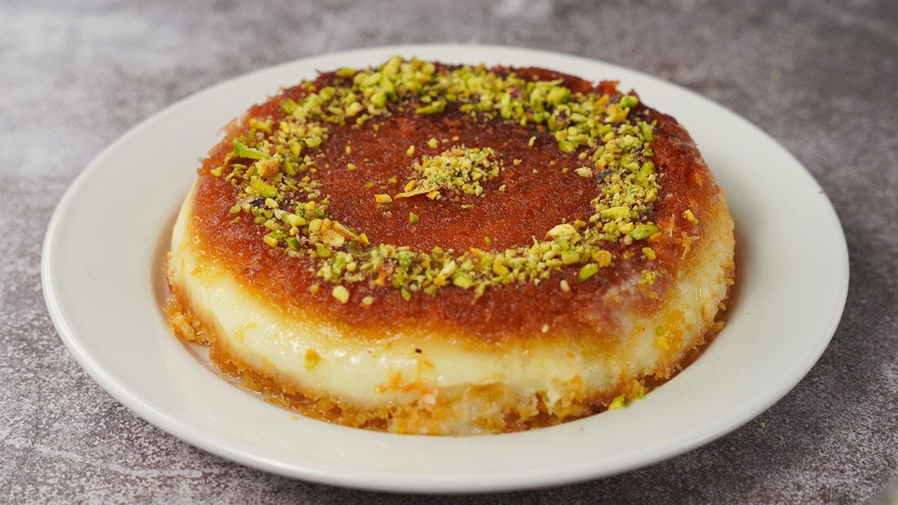 Round serving of kunafa with a golden syrup-soaked pastry top sprinkled with crushed pistachios over a melted white cheese layer