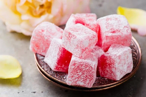 Pink rose Turkish delight cubes dusted with powdered sugar on a small ornate copper plate