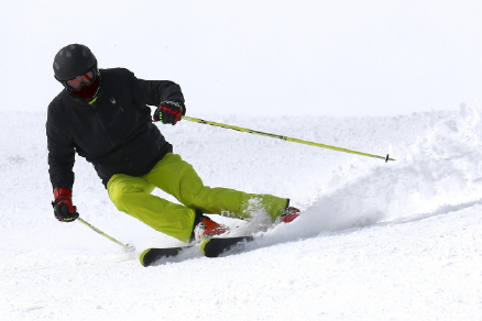 Skier in black jacket and green pants making a sharp turn on snowy slope, kicking up snow.