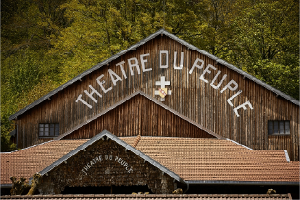 Rustic wooden building with 'THEATRE DU PEUPLE' written on the facade surrounded by trees.