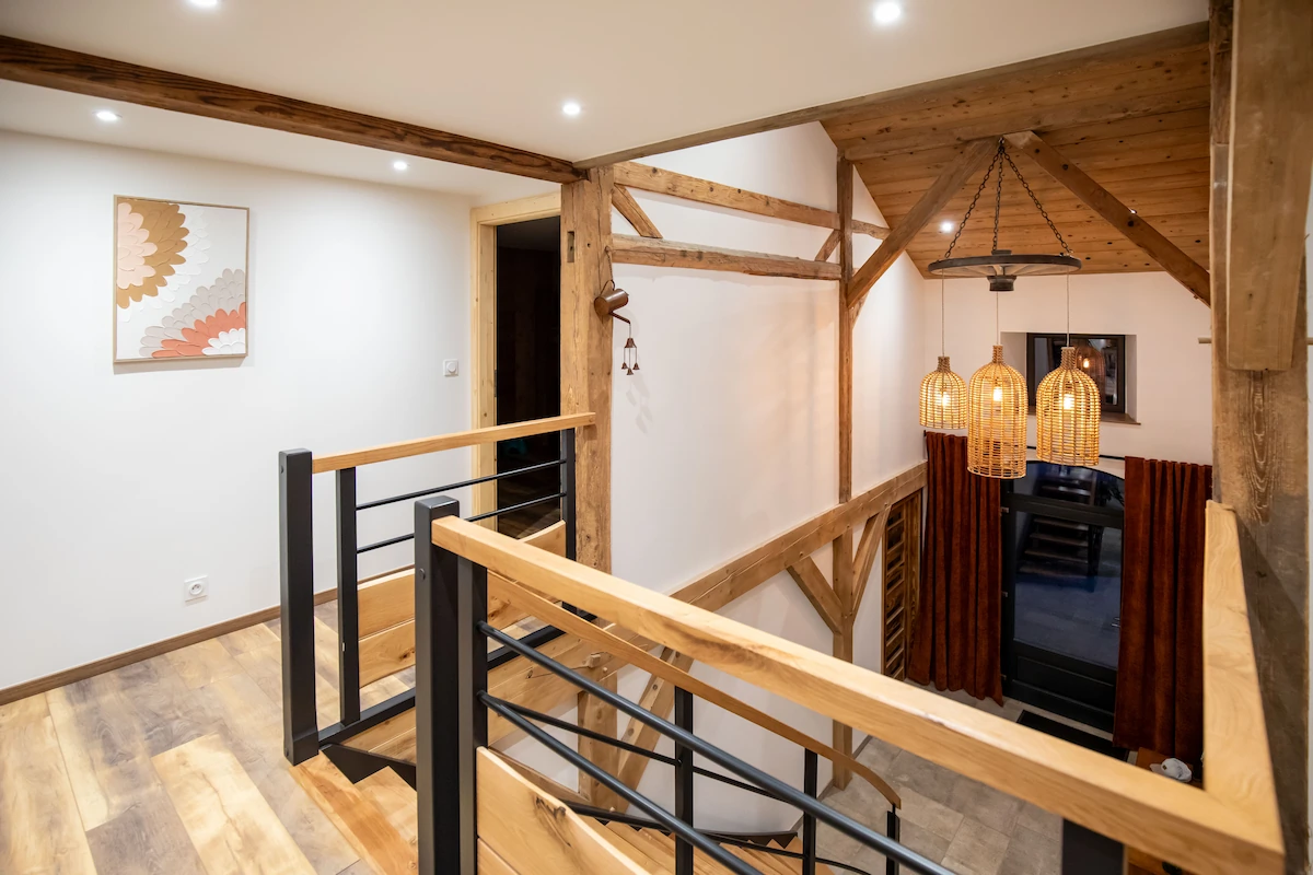 Modern staircase with wooden handrails and black metal balusters in a house featuring wooden beams, hanging wicker pendant lights, and white walls.