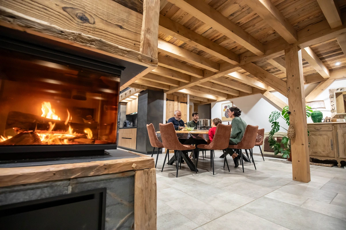 Cozy family of four sitting around a dining table in a rustic room with a wooden beam ceiling and a fireplace.
