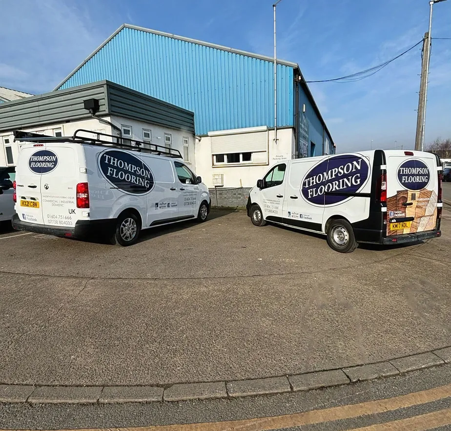 A couple of Thompson Flooring vans parked in a parking lot.