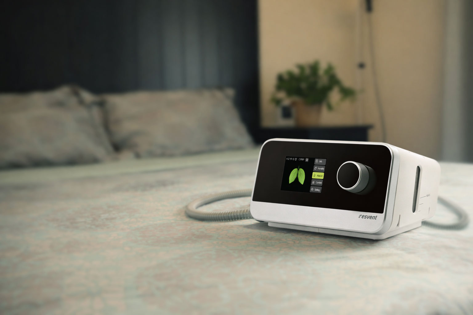 Resvent CPAP machine with a digital display showing lung icons, placed on a bed with a patterned bedspread.