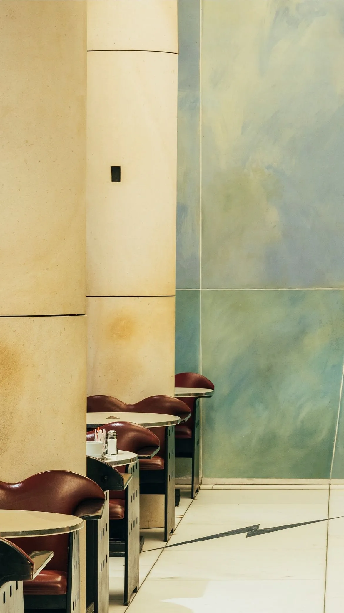 Alignement de tables rondes avec chaises marron foncé dans un restaurant au mur beige et bleu vert.