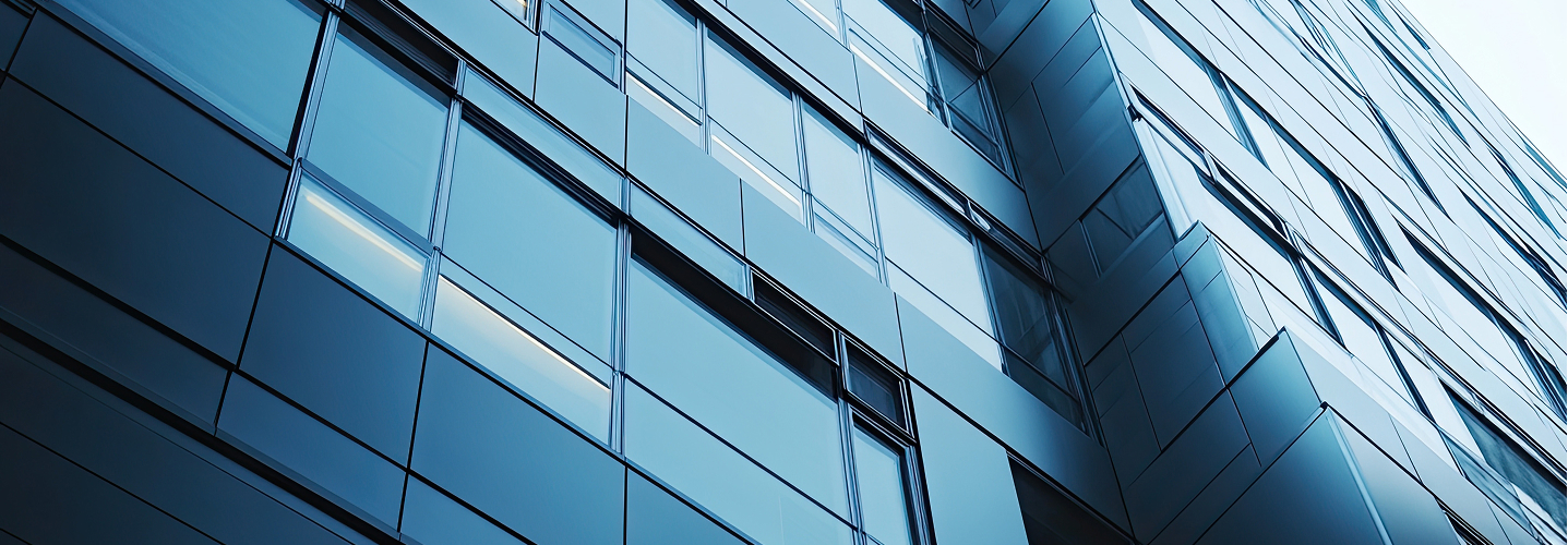 Low-angle view of a modern glass office building's geometric blue facade.
